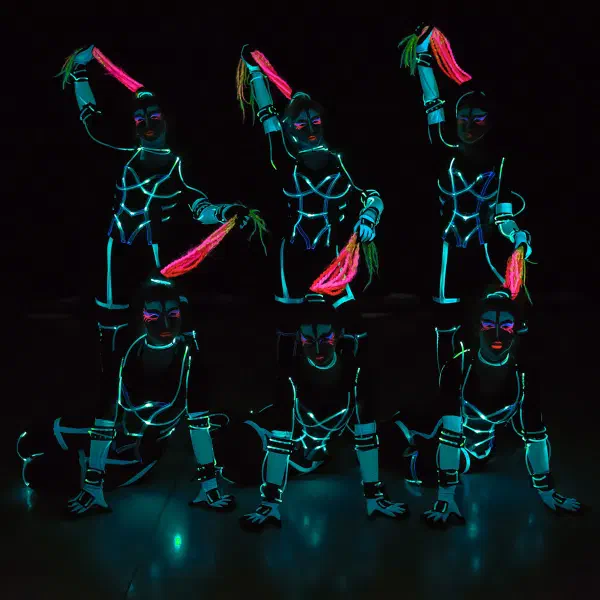 Tron Girls: šesť LED tanečníc v tyrkysových neónových kostýmoch v dvoch radoch drží nad sebou ružové a žlté vrkoče