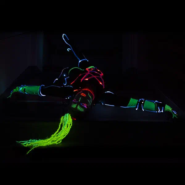 Tron Girls: LED tanečnica v záklone na tmavých schodoch s neónovo zelenými vrkočmi a červenými a modrými svetelnými drôtmi