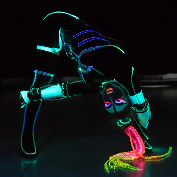 Tron Girls: LED tanečnica v hlbokom záklone v tyrkysovom neónovom kostýme, ružové a žlté vrkoče sa dotýkajú zeme