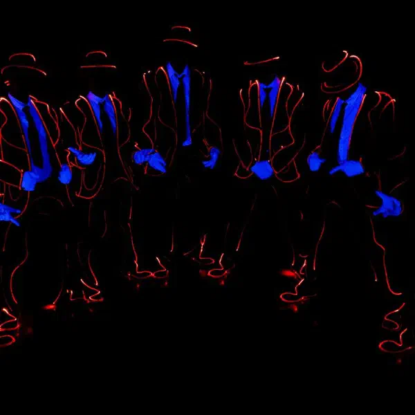 Tron Man: seven dancers outlined in red light wire with fedoras, UV-blue gloves and ties in an LED & UV dance show