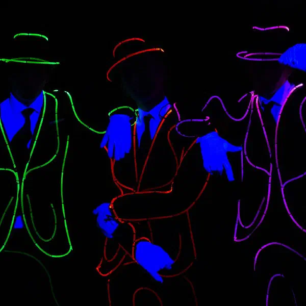 Tron Man: three dancers in green, red and violet light-wire suits and hats with glowing UV-blue gloves