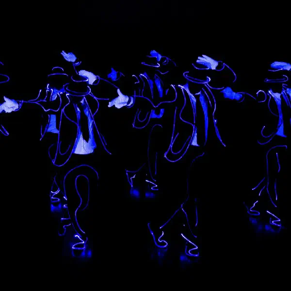 Tron Man: six dancers outlined in blue light wire tipping their fedoras in a moving line on a black stage
