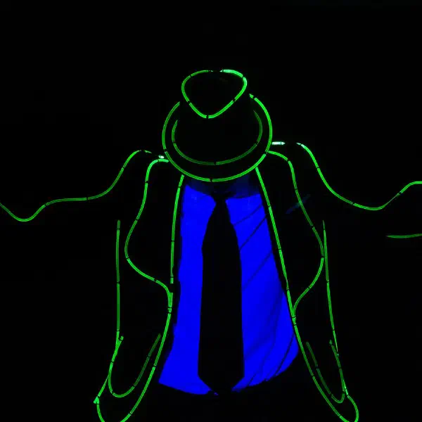 Tron Man: solo dancer in a green light-wire suit and fedora with arms wide, blue UV shirt and gloves glowing