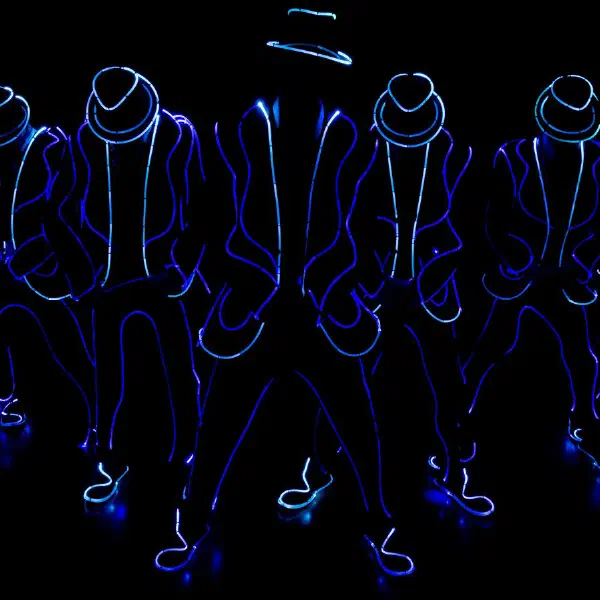 Tron Man: seven dancers in blue light-wire suits and fedoras in a V formation, heads bowed, on a dark stage