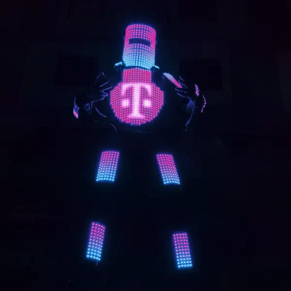 Tron Pixel Robot showing the magenta Deutsche Telekom 'T' logo on its chest screen, with pink and blue pixel LEDs on its helmet, arms and stilts