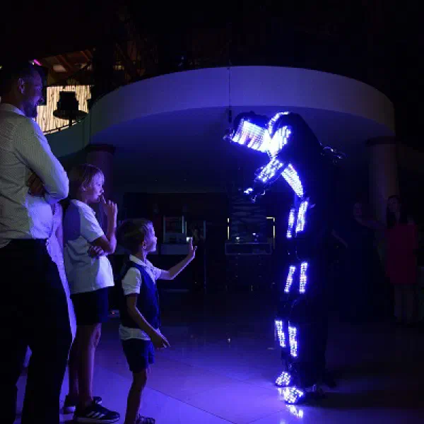 Tron Pixel Robot at a wedding: children and guests watching the robot glowing in white and blue pixels, one boy reaching out to it