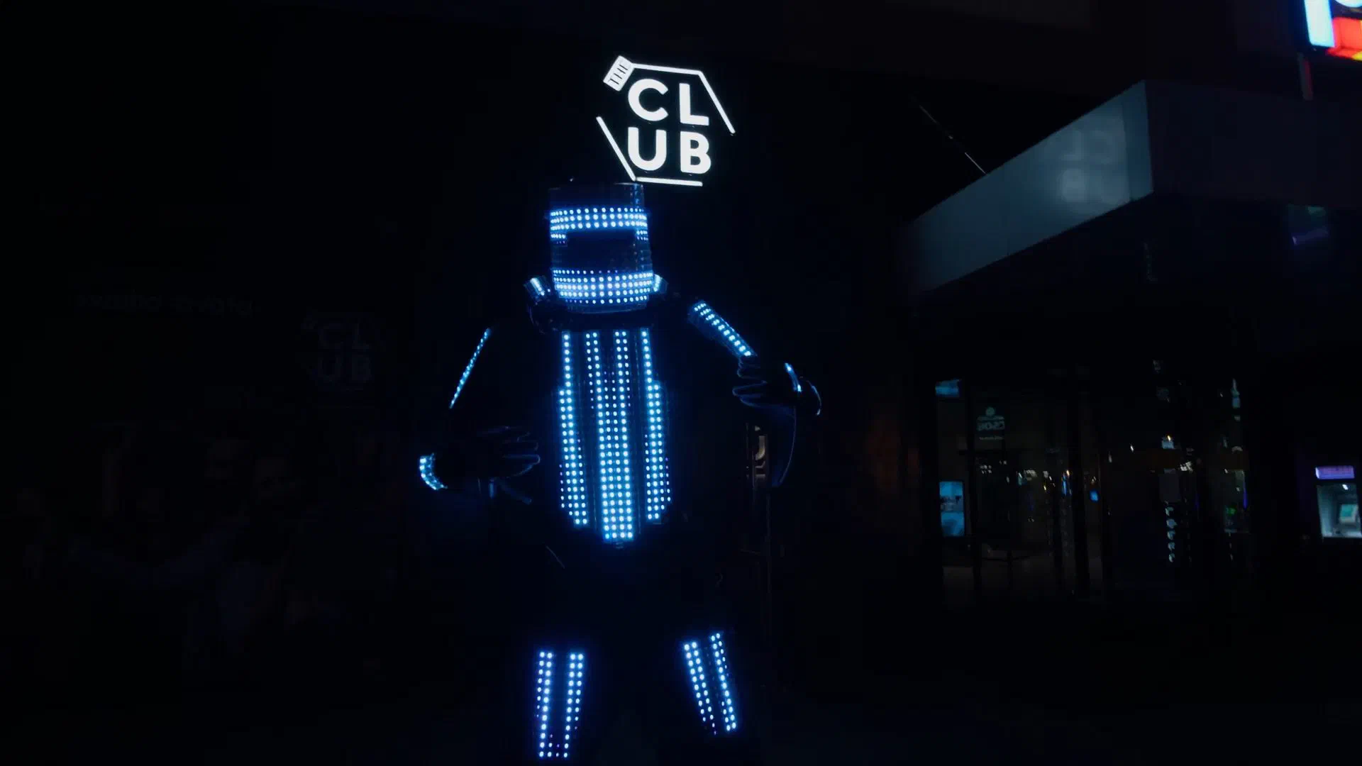 Tron Pixel Robot: an LED robot stilt walker with glowing blue pixel panels, posing at night in front of an illuminated club sign