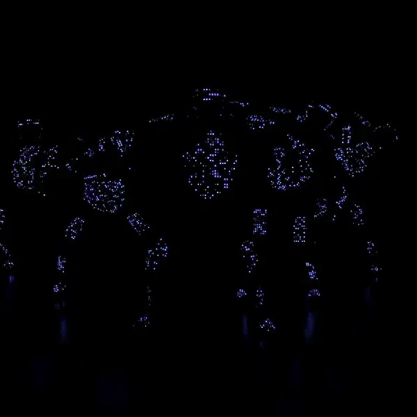 Tron Pixel Show: pixeloví LED tanečníci v tesnej skupine s jemnými fialovými bodkovými vzormi na kostýmoch v takmer úplnej tme