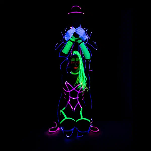 Wedding Show: performer in a hat and blue neon suit holding his hands above a female partner with green braids