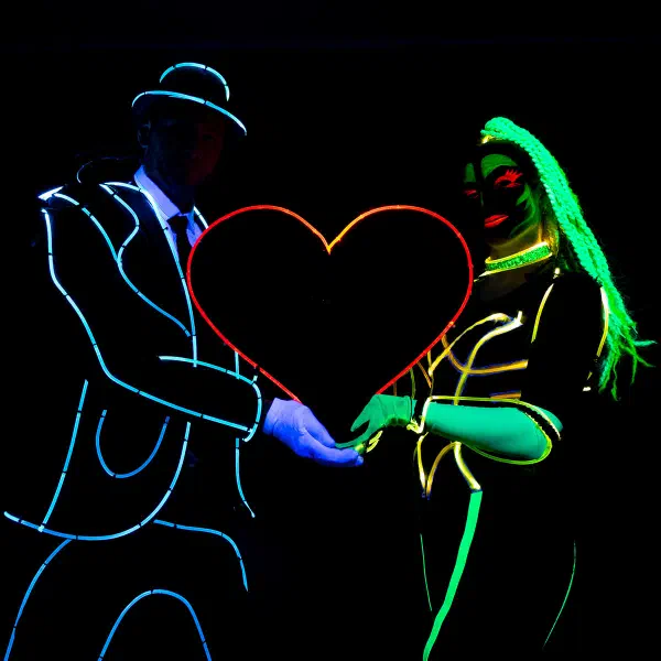 Wedding Show: couple in blue and green neon costumes holding a large red light-up heart between them