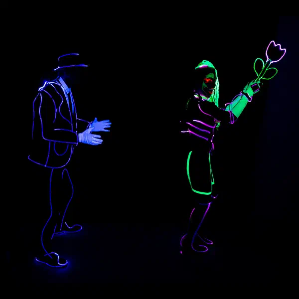 Wedding Show: man in a violet neon suit reaching towards a woman holding up a glowing tulip in a wedding light show