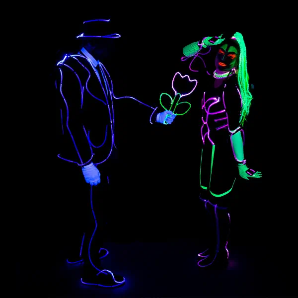 Wedding Show: man in a violet neon suit handing a glowing tulip to a woman in pink and green neon with UV make-up