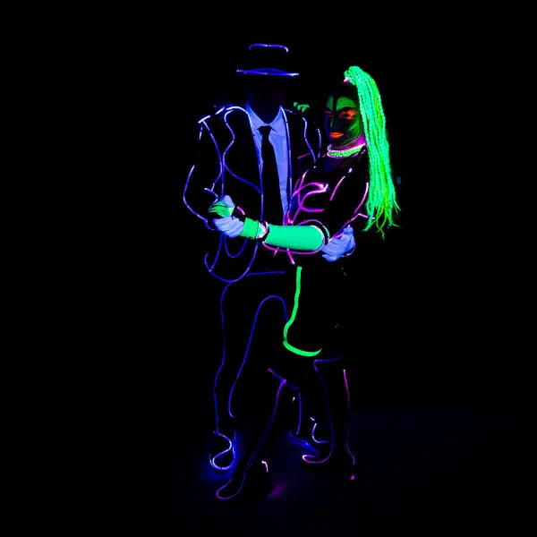 Wedding Show: couple in violet and green neon wire costumes embracing in a dance pose against a black backdrop