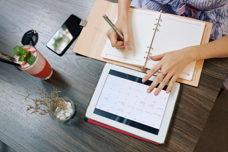 Close-up of a woman planning an event using a tablet calendar and notebook, demonstrating effective scheduling and organization skills for event planning