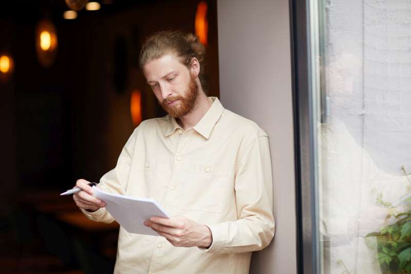 Thoughtful man standing by a window, reviewing notes on a clipboard—capturing the focused mindset and attention to detail needed to succeed as an event planner