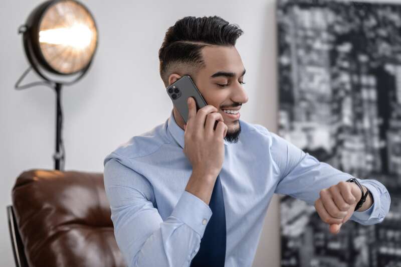 Smiling young professional talking on the phone while checking his watch, representing time management and communication—key skills for successful event planners.